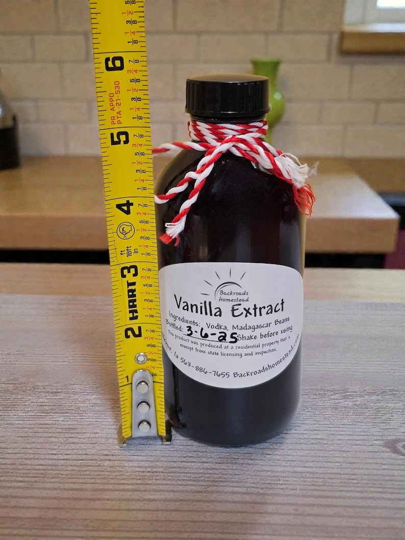 May include: A dark glass bottle of vanilla extract, approximately 5 inches tall, with a black cap and a red and white twine tie. The label reads "Vanilla Extract" and lists ingredients and bottling date.