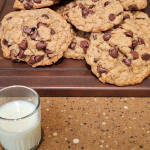 Puede incluir: Una pila de galletas con chispas de chocolate reci&eacute;n horneadas y un vaso de leche. Las galletas son de color marr&oacute;n dorado con chispas de chocolate. El vaso est&aacute; lleno de leche blanca.