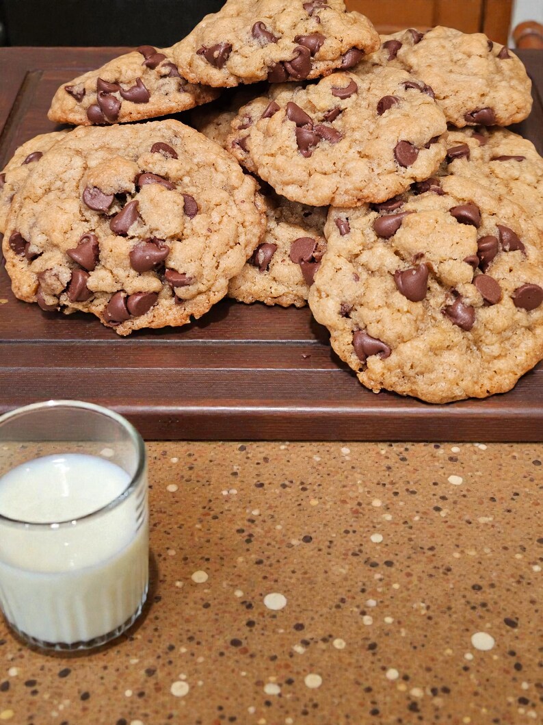 Puede incluir: Una pila de galletas con chispas de chocolate reci&eacute;n horneadas y un vaso de leche. Las galletas son de color marr&oacute;n dorado con chispas de chocolate. El vaso est&aacute; lleno de leche blanca.