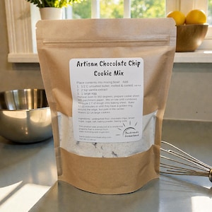 Könnte beinhalten: Ein brauner Papiersack mit "Artisan Chocolate Chip Cookie Mix" mit Anweisungen und Zutaten. Der Sack steht auf einer Küchentheke, mit Schneebesen und Schüssel im Hintergrund. Nettogewicht: 382 Gramm.