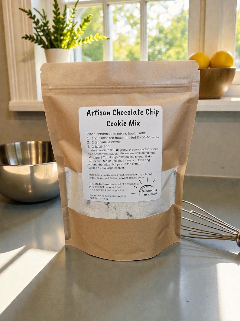 Puede incluir: Una bolsa de papel marr&oacute;n con "Mezcla de galletas con chispas de chocolate artesanal" con instrucciones e ingredientes. La bolsa est&aacute; sobre una encimera con un batidor y un cuenco. Peso neto: 382 gramos.