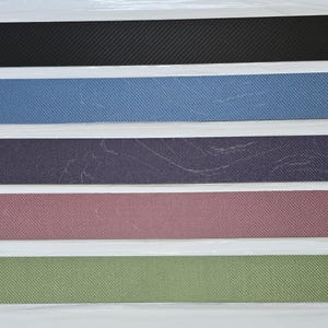 May include: Five fabric samples in different colors and textures. The samples are arranged vertically, with the black sample at the top and the green sample at the bottom. The samples are all approximately the same size and shape.