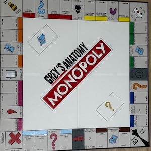 May include: A custom-made Monopoly board game with a Grey's Anatomy theme. The board features spaces like "Operating Room", "Blood Bank", and "Scrub Room". The game board is white with red, blue, and green accents.