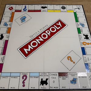 May include: A white Monopoly board game with a red and black title card that reads "Gavin & Stacey Monopoly". The board is set up with property spaces, chance cards, community chest cards, and a "Go" space.