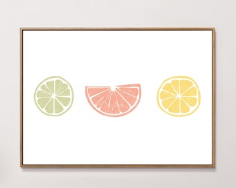 May include: A digital print featuring three stylized citrus fruit slices in shades of green, pink, and yellow. The print is framed in a light wood frame and is hanging on a white wall.
