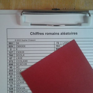 Puede incluir: Un portapapeles blanco con una carpeta roja encima. El portapapeles tiene una lista de números y sus equivalentes en números romanos. El texto en el portapapeles dice "Chiffres romains aléatoires" y "© 2023 Sophie Chiasson".