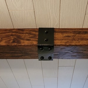 May include: A dark brown wooden beam with a black metal bracket attached to the top. The bracket has five round black metal rivets.