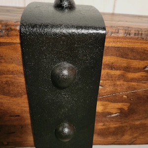 May include: Black metal bracket with three round decorative accents. The bracket is attached to a wooden beam.