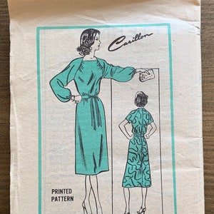 May include: Vintage sewing pattern for a dress, featuring a woman in a teal dress with a belt. The pattern is labelled "Carillon Prominent Designer M 320 - SIZE 14 PRINTED PATTERN".
