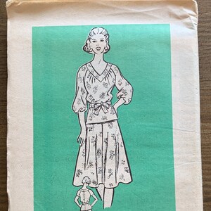 Puede incluir: Patrón de costura vintage para un conjunto de blusa y falda. El patrón está impreso en papel y presenta una ilustración en blanco y negro de una mujer vistiendo el atuendo. El número del patrón es 4930 y la talla es 14 1/2.
