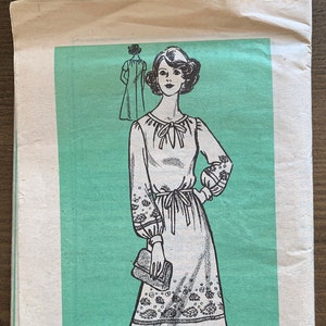 May include: A vintage sewing pattern for a dress with a tie at the neck and long sleeves. The pattern is printed on a green background and includes the number 9472 and the size 18 1/2.