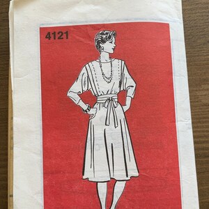 Può includere: Un cartamodello vintage per un abito, con un'illustrazione in bianco e nero di una donna che indossa un abito con una cintura a fiocco. Il numero del cartamodello è 4121 e la taglia è (12-14-16-18) (20-22-24-26).