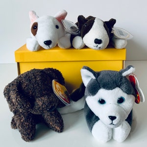 Pode incluir: Quatro cães de pelúcia em uma caixa amarela. Os cães são um bull terrier branco e marrom, um bull terrier marrom e branco, um labrador retriever marrom e um husky cinza e branco.