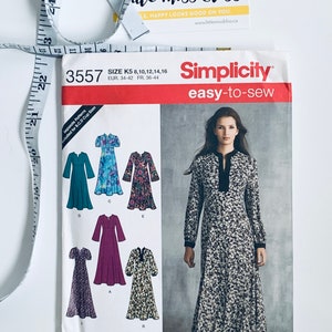 Peut inclure: Un patron de couture Simplicity facile à coudre, taille K5, présentant des modèles de robes. Le patron comprend les tailles 34 à 44. Un mètre ruban et une carte de visite sont également visibles.