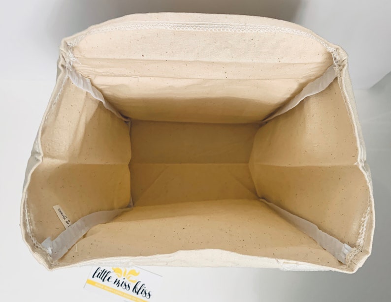 May include: A white canvas tote bag with a white fabric lining. The bag has a label on the bottom that says "little miss bliss".