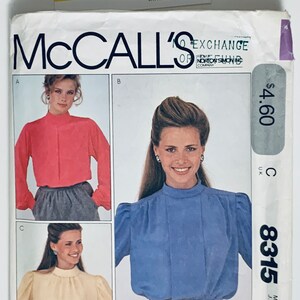 Pode incluir: Um padrão de costura vintage da McCall's para uma blusa feminina. O padrão é para o tamanho 20 e inclui três vistas diferentes: uma blusa vermelha de manga comprida, uma blusa azul de manga comprida e ombros bufantes, e uma blusa creme de manga comprida e ombros bufantes. O padrão é etiquetado como "8315" e tem um preço de $ 4,60.