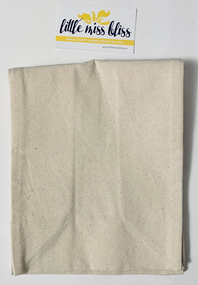 May include: A beige canvas fabric with a speckled texture. The fabric is folded in half and appears to be a piece of material for crafting or sewing projects.