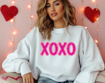 May include: A white sweatshirt with a pink glitter XOXO graphic.