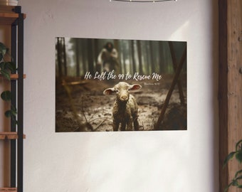 May include: A framed print featuring a lamb in a forest setting. The image has a soft, muted color palette with the text "He Left the 99 to Rescue Me" and "Matthew 18:12". The background shows a blurred figure in the woods.