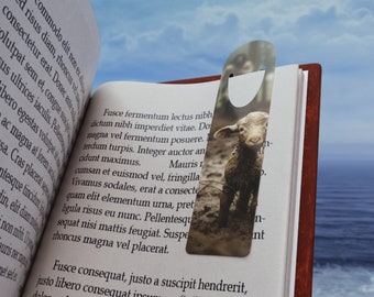 May include: A silver metal bookmark shaped like a bottle opener with a black and white photo of a lamb standing in a field. The bookmark is placed on a book with text about a lamb.