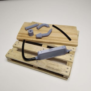 May include: A set of gray plastic model car parts, including a radiator, exhaust pipes, and a hose. The parts are arranged on a wooden pallet.