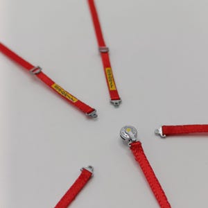 May include: Five red racing harnesses with silver buckles and yellow text. The harnesses are laid out on a white surface.
