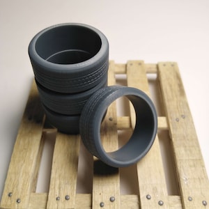 May include: Four gray rubber tires stacked on a wooden pallet. The tires are round and have a tread pattern.