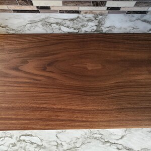 Op de afbeelding: Een rechthoekige houten snijplank met een diepbruine kleur en zichtbare houtnerf. De plank is glad en lijkt van walnoot te zijn. Dit is een keukenartikel.