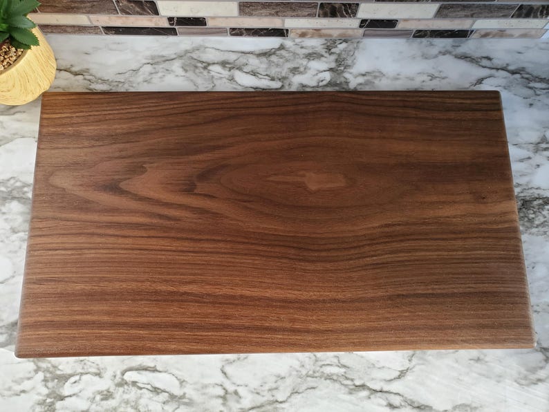 Op de afbeelding: Een rechthoekige houten snijplank met een diepbruine kleur en zichtbare houtnerf. De plank is glad en lijkt van walnoot te zijn. Dit is een keukenartikel.