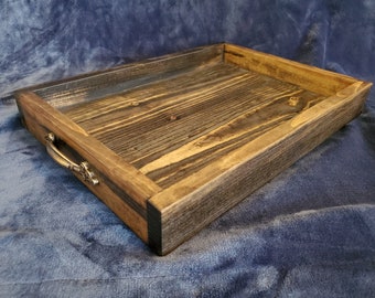 May include: A rustic wooden tray with a dark brown stain and a natural wood grain. The tray has a rectangular shape and features two brass handles on the side.