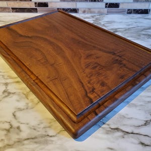 Op de afbeelding: Een rechthoekige houten snijplank met een donkerbruine afwerking. De plank heeft een verzonken sapgroef rondom en een glad, gepolijst oppervlak. De houtnerf is zichtbaar, wat bijdraagt aan de natuurlijke uitstraling.