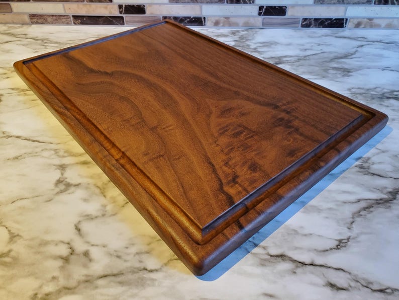 Op de afbeelding: Een rechthoekige houten snijplank met een donkerbruine afwerking. De plank heeft een verzonken sapgroef rondom en een glad, gepolijst oppervlak. De houtnerf is zichtbaar, wat bijdraagt aan de natuurlijke uitstraling.