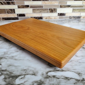 May include: A rectangular wooden chopping board with a natural wood finish. The board has a smooth surface and rounded edges.