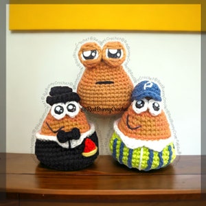 May include: Three crocheted amigurumi plushies in the shape of potatoes. The plushies are wearing different outfits. One is wearing a black suit with a bow tie and a top hat. Another is wearing a blue and white striped shirt with a blue baseball cap. The third plush is wearing a brown shirt with a neutral expression.