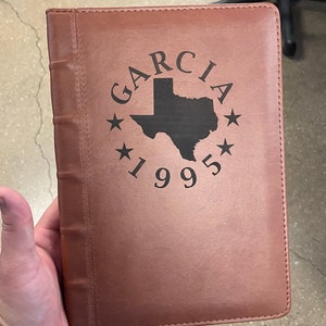 May include: A brown leather journal with a black engraved design featuring the text "GARCIA 1995" and an outline of the state of Texas.