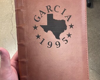 May include: A brown leather journal with a black engraved design featuring the text "GARCIA 1995" and an outline of the state of Texas.