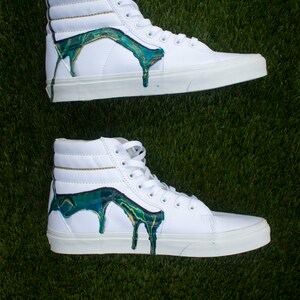 May include: White high-top trainers with green and gold paint dripping down the sides.