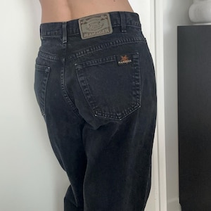 May include: Dark grey denim jeans with a faded look. The back pockets display the brand name "Manager". A leather patch above the right back pocket also shows the brand name. The jeans have a classic five-pocket design.