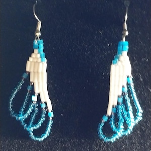 May include: A pair of handmade beaded earrings. The earrings feature a white and turquoise color scheme. The top portion is a stacked white design with turquoise accents. The bottom has turquoise beaded loops, creating a flowing, elegant look.