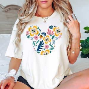 Op de afbeelding: Wit T-shirt met een bloemig Mickey Mouse ontwerp in geel, roze, blauw en groen.
