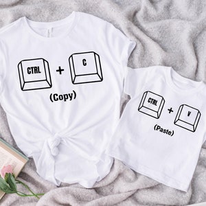 May include: Two white t-shirts with a computer keyboard design. The larger shirt says "CTRL + C (Copy)" and the smaller shirt says "CTRL + V (Paste)".