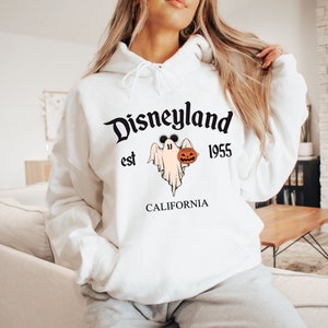 May include: White hoodie with the text "Disneyland est 1955 CALIFORNIA". The graphic features a ghost wearing Mickey Mouse ears and holding a jack-o'-lantern. A Halloween-themed sweatshirt.