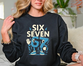 May include: Black sweatshirt with the text "SIX SEVEN" in a retro font. Below the text is a cartoon-style illustration of the numbers 6 and 7 in blue, with arms, legs, and shoes. The design includes lightning bolt accents.