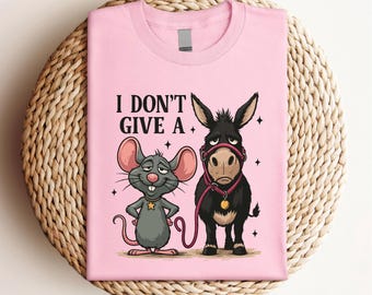 May include: Pink t-shirt featuring a cartoon mouse and donkey with the text "I DON'T GIVE A." The mouse is gray with a gold star, and the donkey is black with a pink halter. The shirt is displayed on a woven surface.
