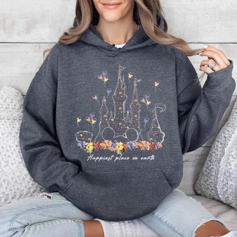 May include: A dark gray hoodie with a white outline of Cinderella's castle filled with floral designs. The text "Happiest place on earth" is printed below the castle.