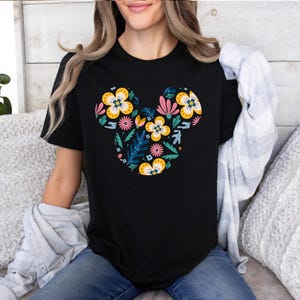 Op de afbeelding: Zwart T-shirt met een bloemig Mickey Mouse ontwerp. Het ontwerp bevat gele, roze, blauwe en groene bloemen.
