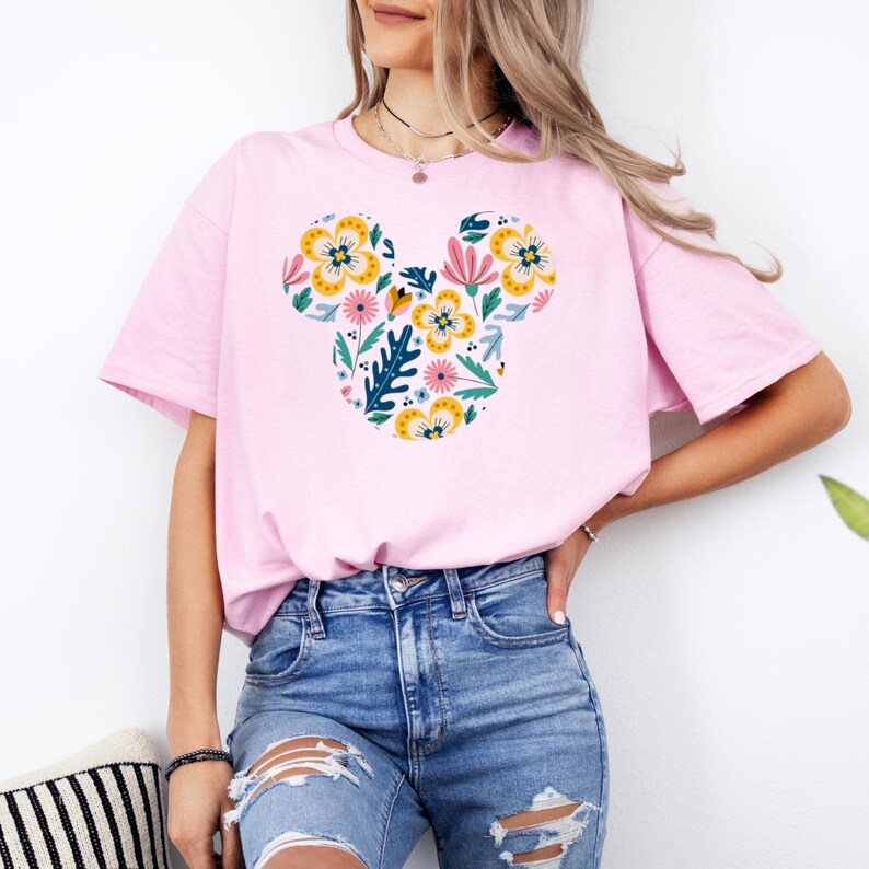 Op de afbeelding: Een roze T-shirt met een bloemig Mickey Mouse-ontwerp. Het ontwerp bevat gele, roze, blauwe en groene bloemen.