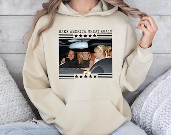 May include: A beige hoodie with a black graphic print of three women in a car. The graphic includes the text "MAKE AMERICA GREAT AGAIN" and five stars.