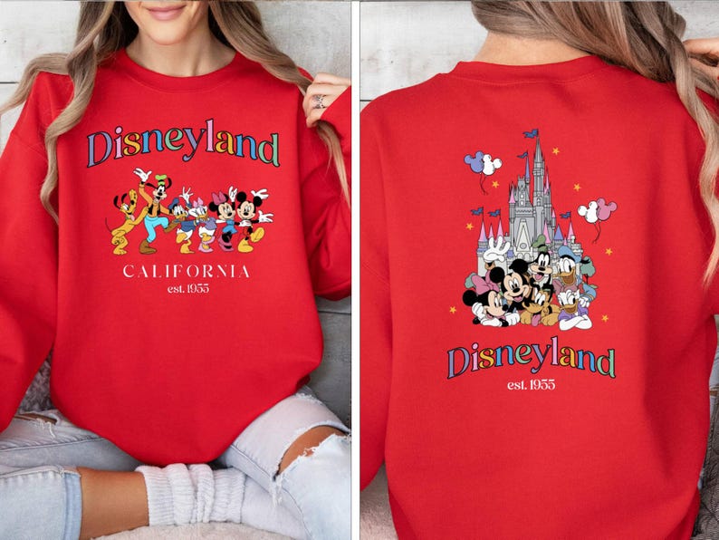 Puede incluir: Sudadera roja con un logotipo de Disneyland colorido y un gr&aacute;fico de Mickey Mouse y sus amigos frente al castillo de Disneyland. El texto en la sudadera dice "Disneyland California est. 1955".