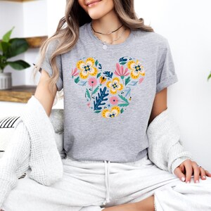 Op de afbeelding: Een grijs T-shirt met een bloemig Mickey Mouse ontwerp. Het ontwerp bevat roze, gele en blauwe bloemen met groene bladeren.